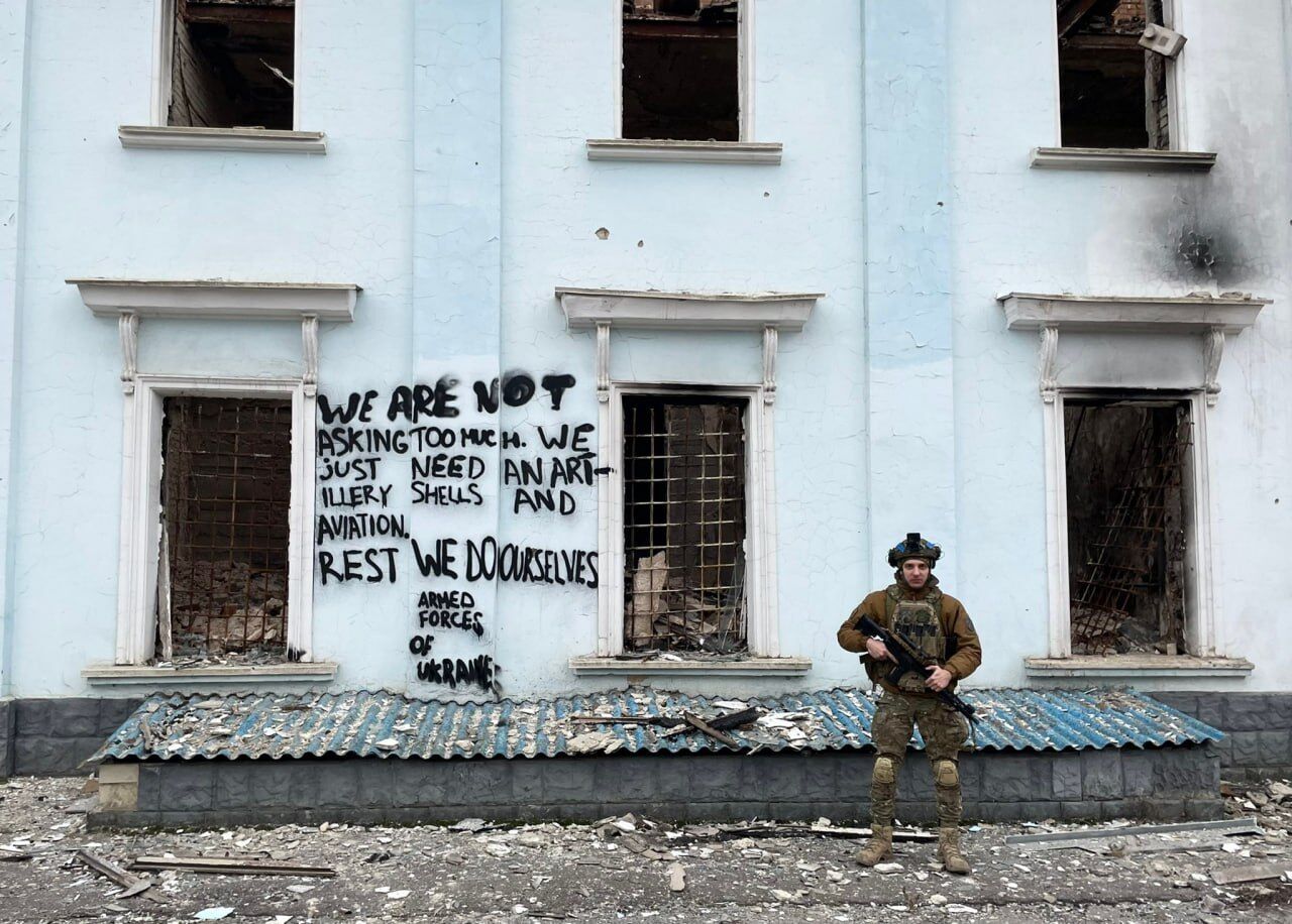 In the photo, a soldier stands against the background of an English-language inscription